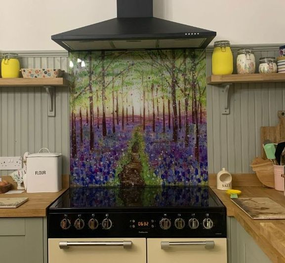 Kitchen stove with black range hood and floral forest backsplash between wooden countertops and shelves
