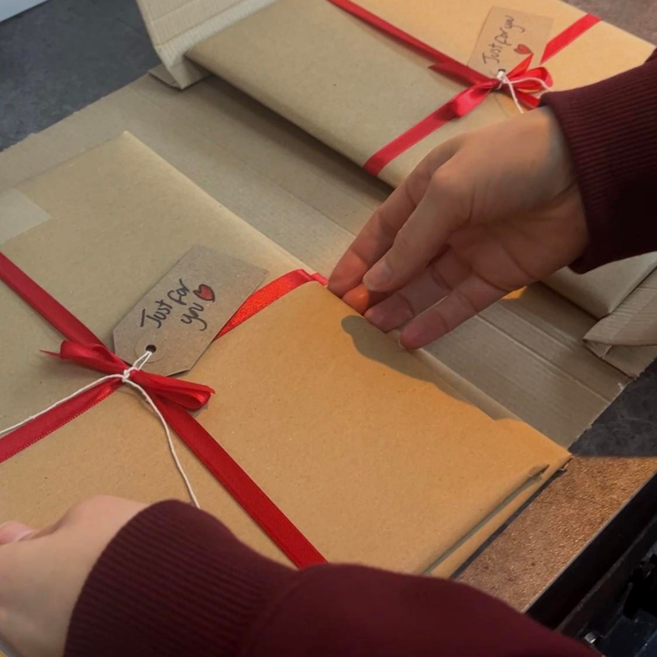 Hands tying red ribbons on wrapped kraft paper gifts on a table