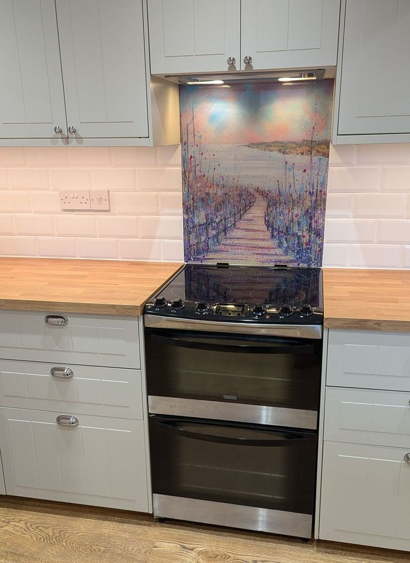 Modern kitchen with a black stove beneath a colorful glass backsplash and light wood counters