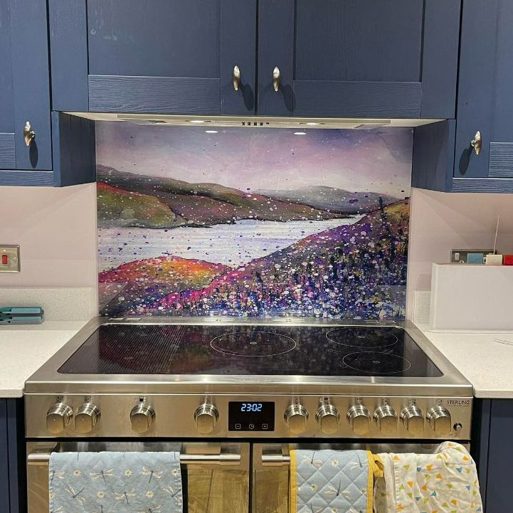 Kitchen stove with a colorful abstract landscape tile backsplash and blue cabinets above it