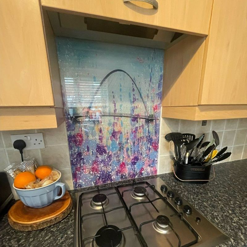 Kitchen countertop with gas hob, bowl of oranges, utensil holder, and patterned backsplash behind the stove
