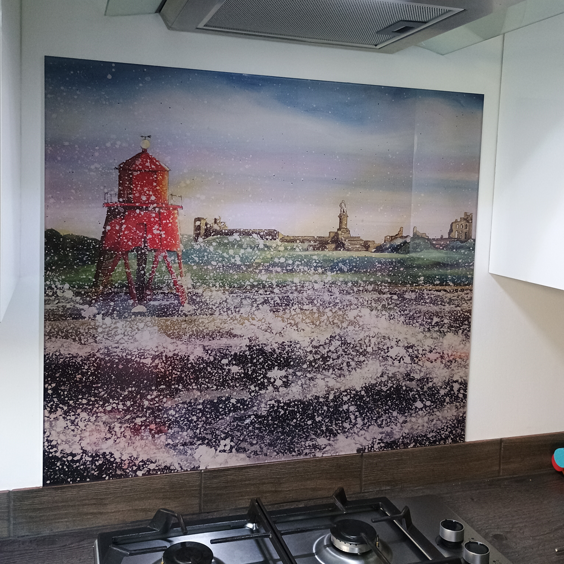 Painting of a red lighthouse by rough sea under a cloudy sky, hung above a kitchen stove