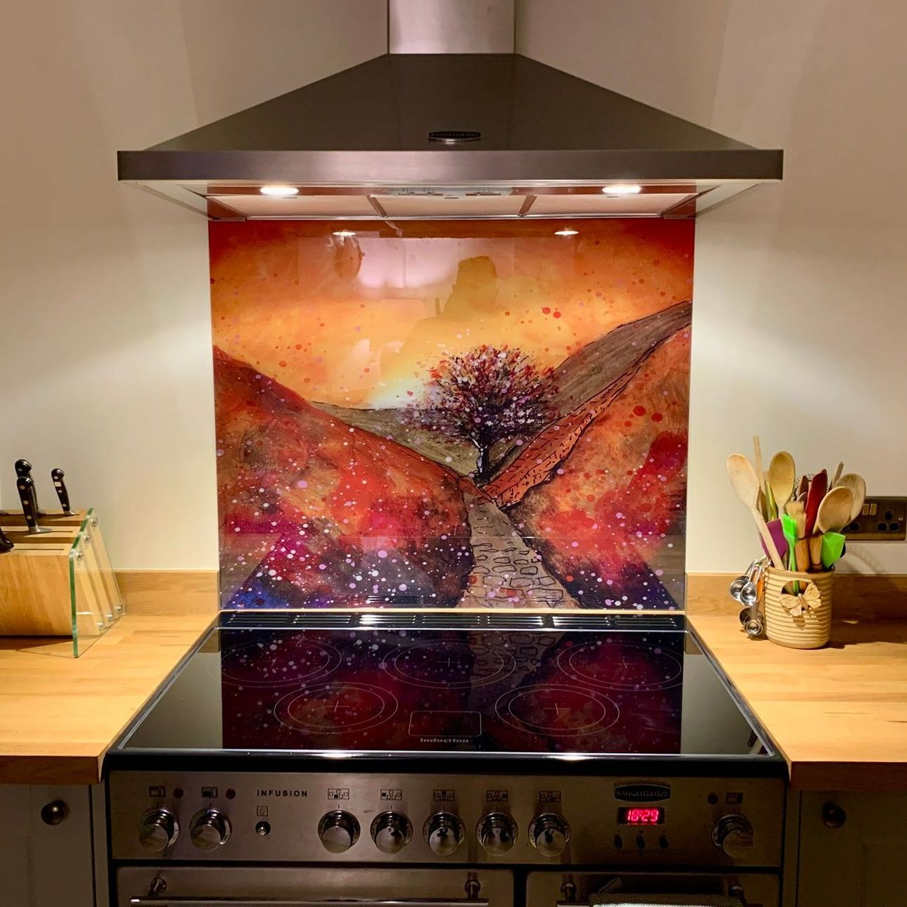 Modern kitchen stove with stainless hood and colorful abstract backsplash lit by under-cabinet lights