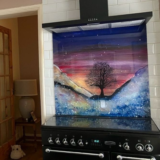 Colorful landscape artwork with a silhouetted tree above a stove in a kitchen