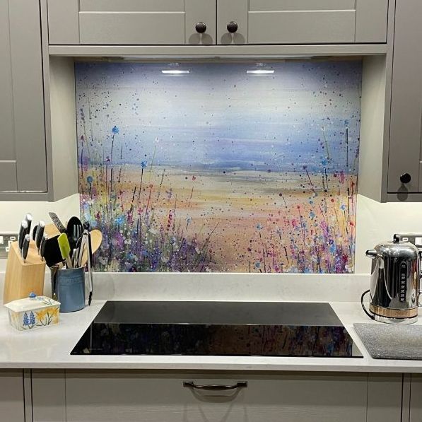 Kitchen with glass cooktop and colorful abstract backsplash art between gray cabinets