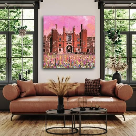 Modern living room with a tan sofa, round coffee tables, and a colorful castle painting between large windows.