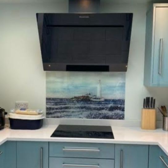 Modern kitchen with blue cabinets, white counters, black range hood, and seascape backsplash art.