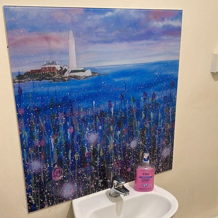Colorful lighthouse painting above a sink with a pink soap dispenser on the counter