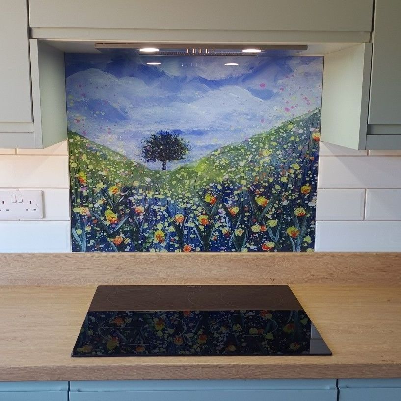 Kitchen countertop with black glass cooktop beneath a colorful floral landscape backsplash painting