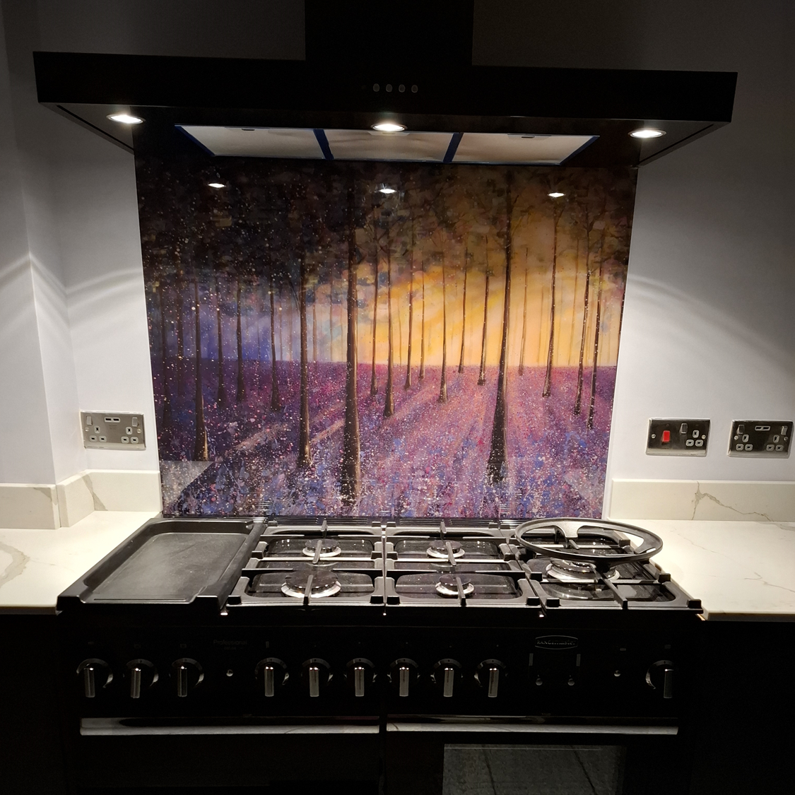 Black range stove beneath a hood, with a colorful purple-and-gold mosaic backsplash.