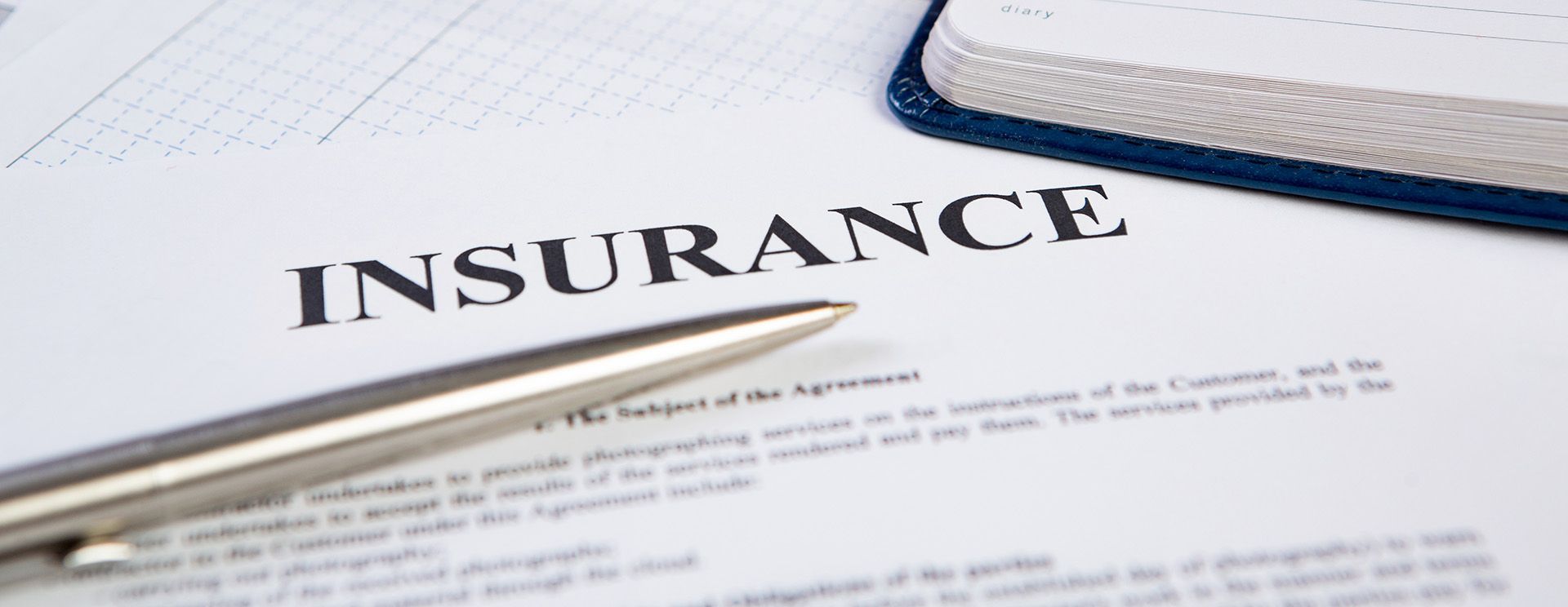Pen resting on an insurance document beside an open notebook.