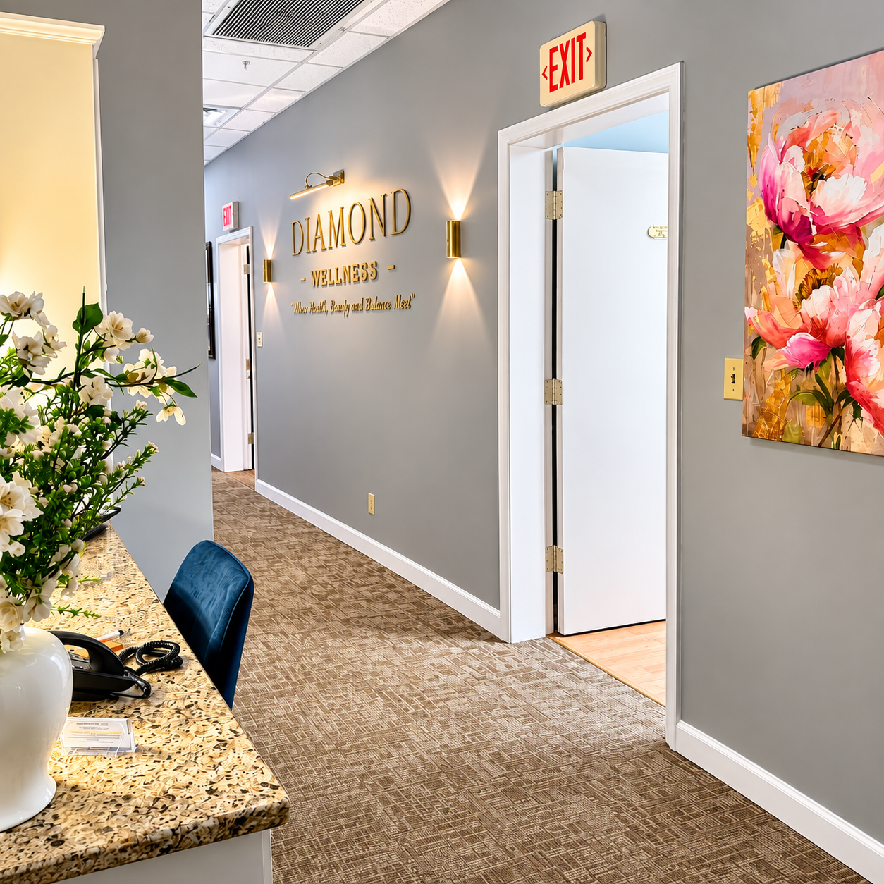 Office hallway with gray walls, carpet, exit sign, flowers, and a reception counter in the foreground