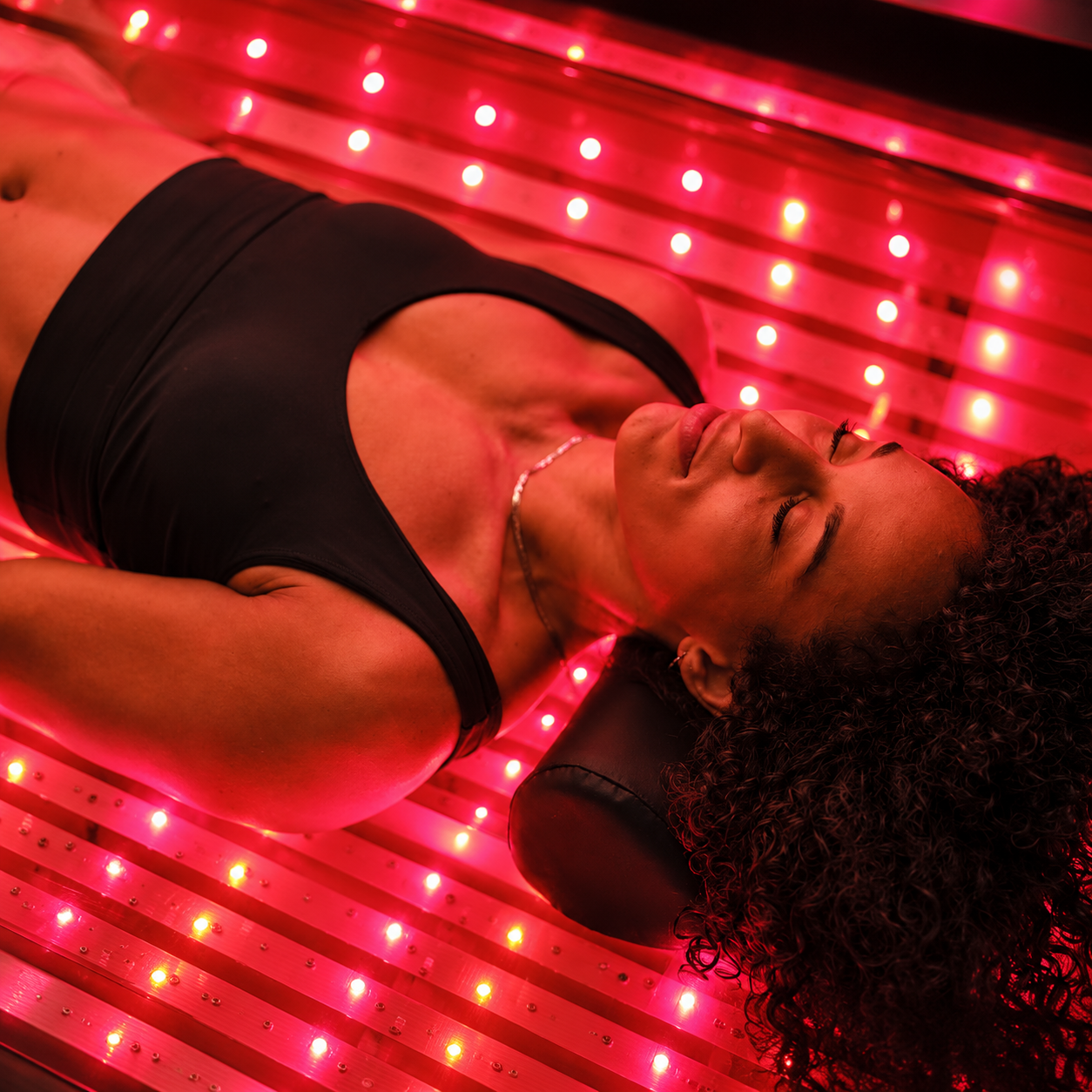 Person reclining on a glowing red LED floor, lit by red light and wearing a black top.