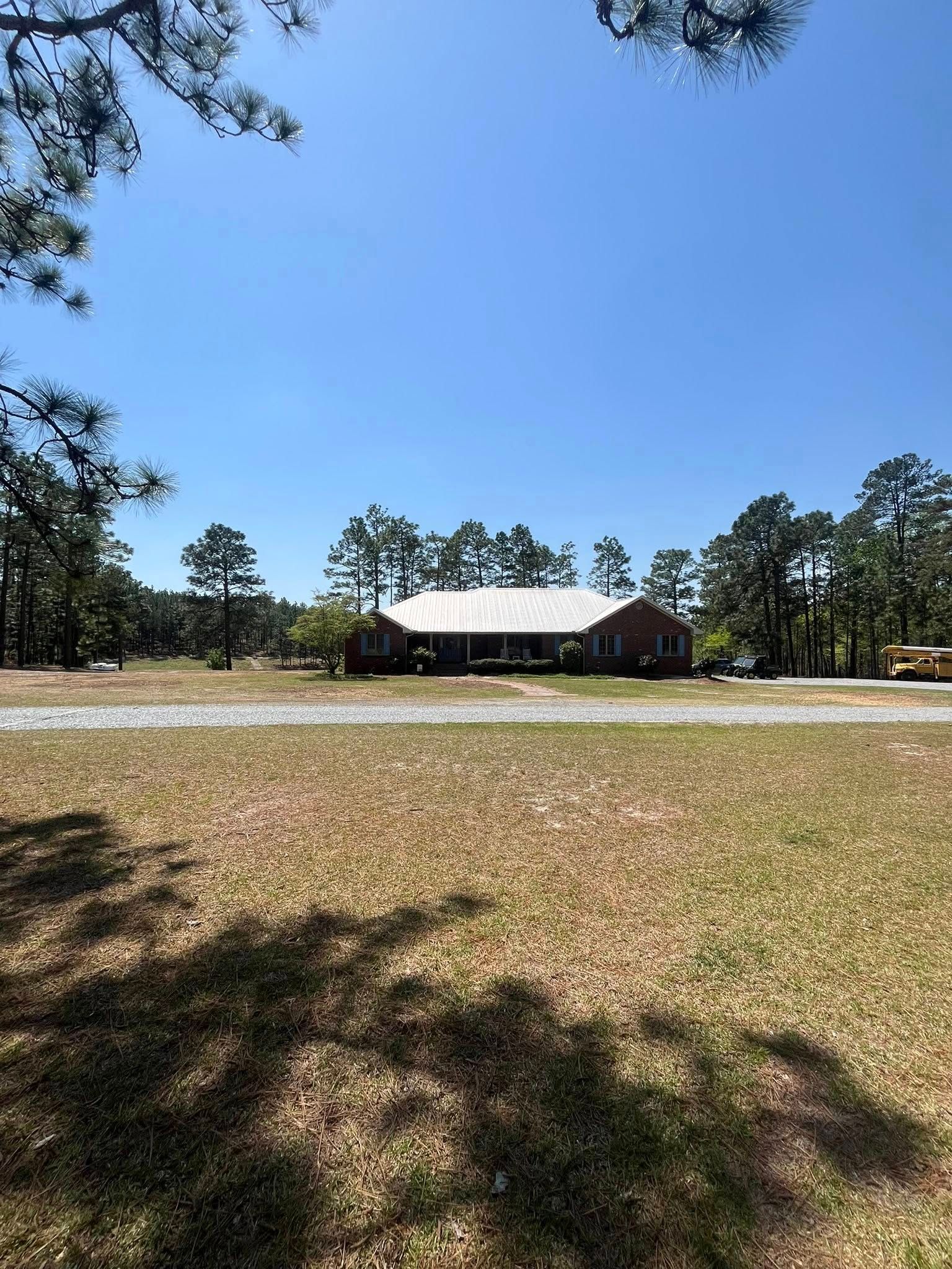 Single-story brick house with a white roof in a grassy field under a clear blue sky.