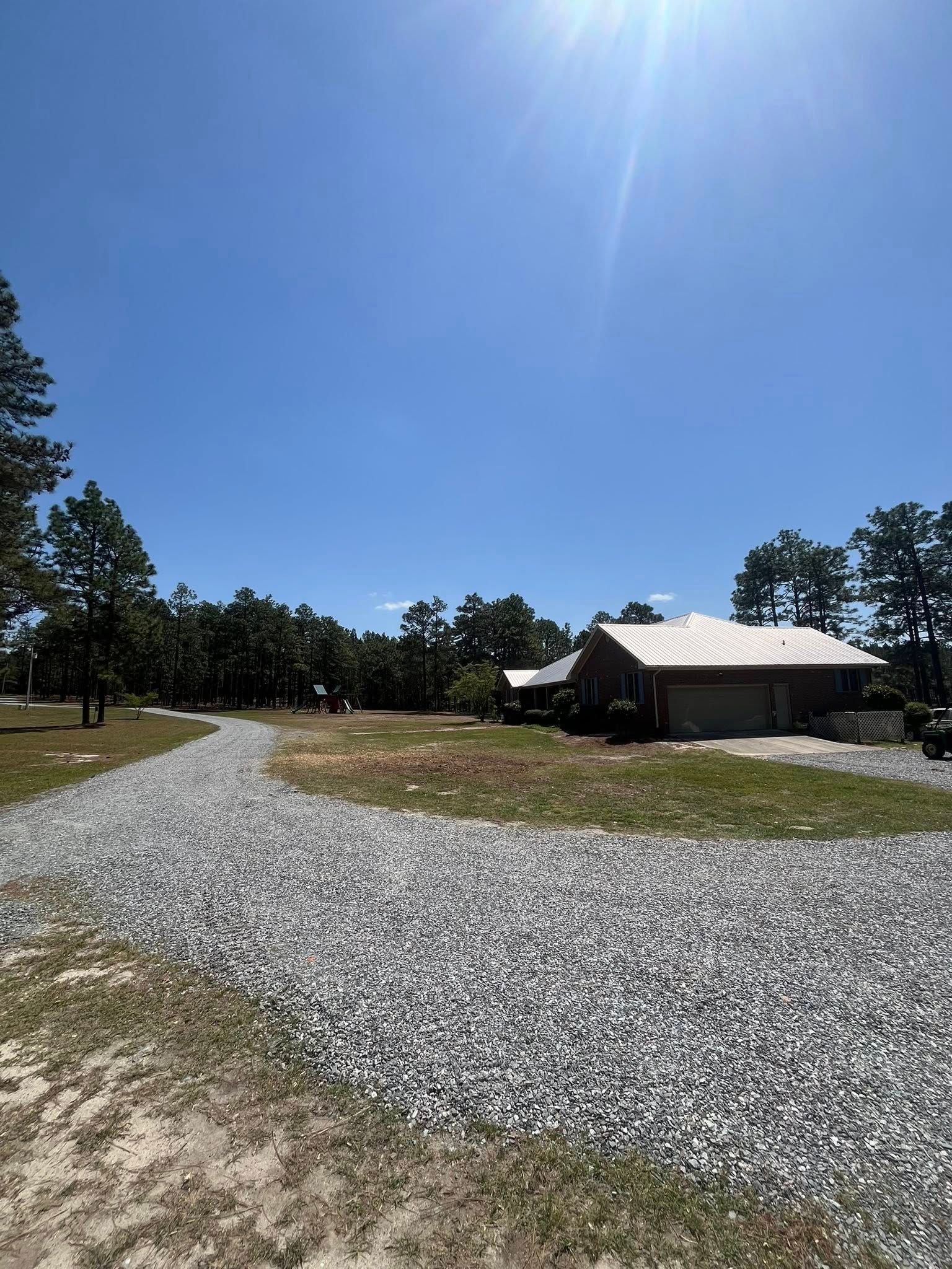 Gravel path curving past a rustic cabin in a sunny grassy field under a clear blue sky