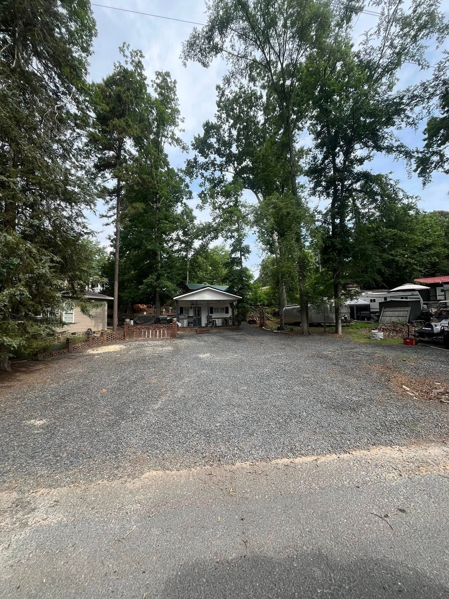 Gravel lot with trees and a small building in the background, under a partly cloudy sky