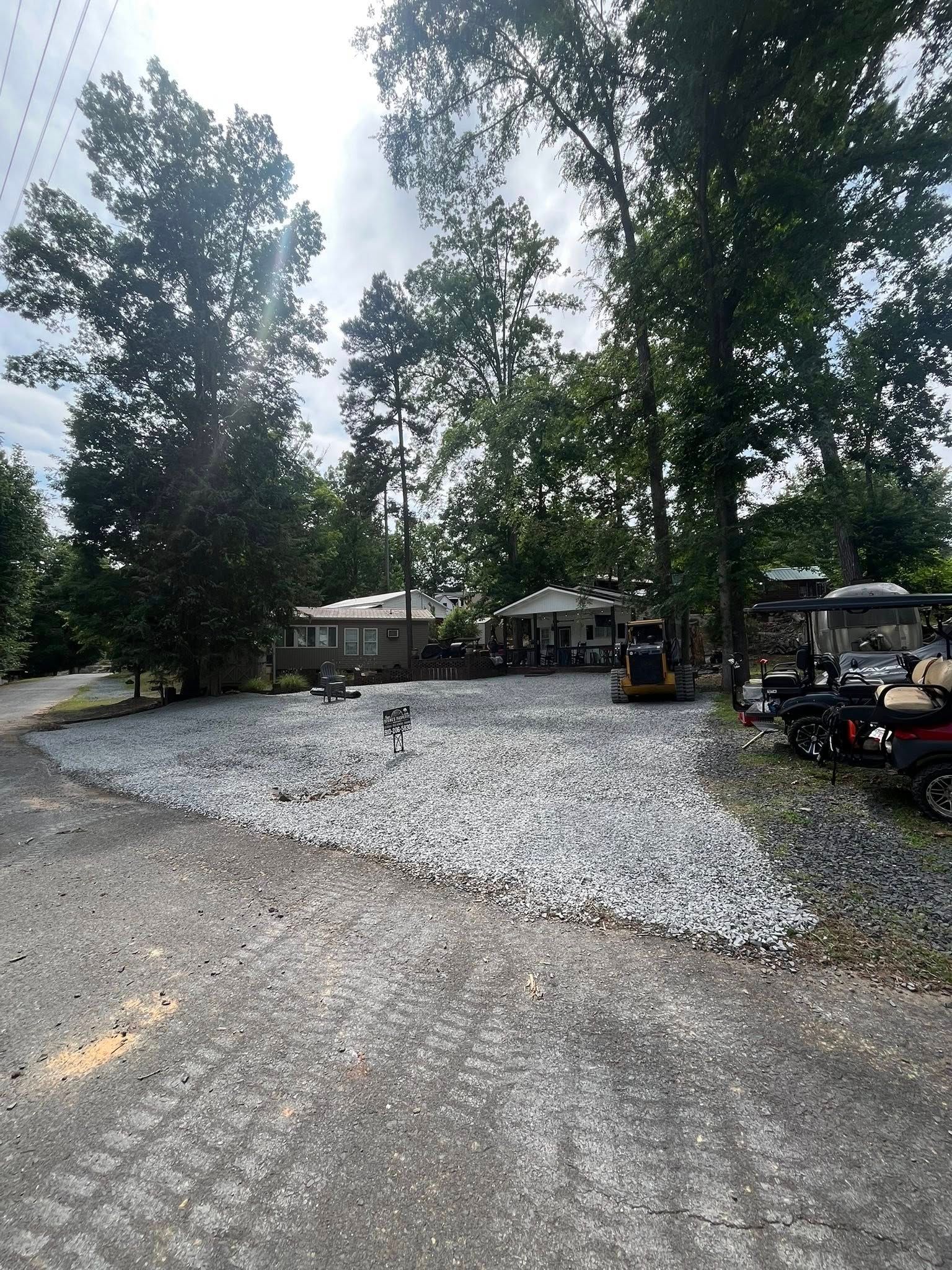 Gravel parking area beside trees and a small building, with a yellow utility vehicle on the right.