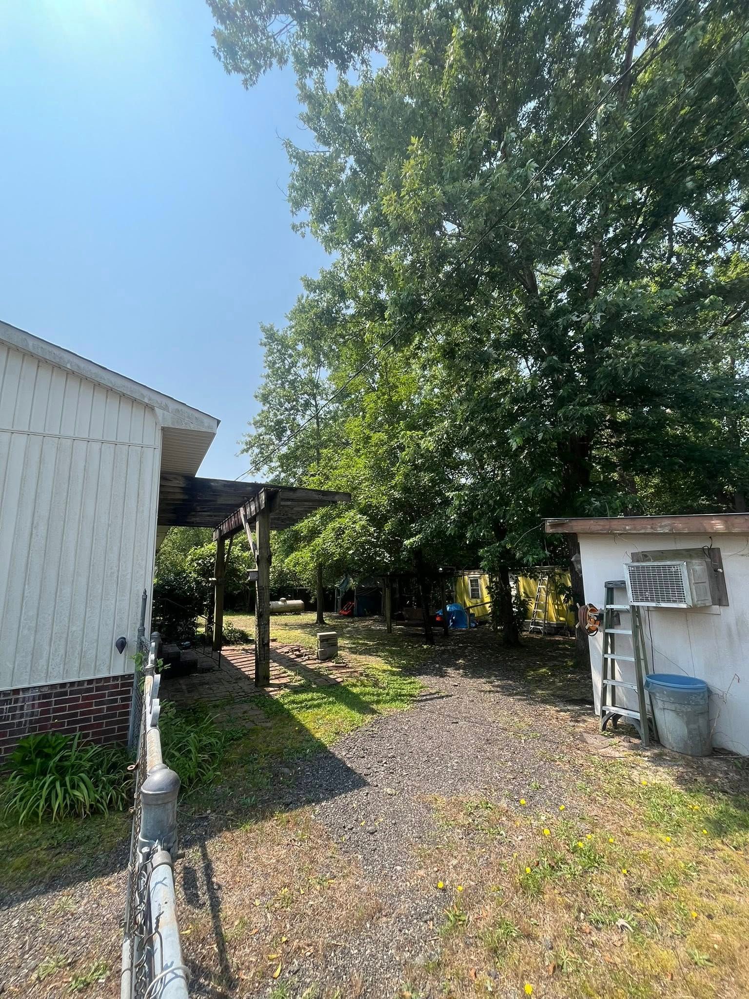 Gravel driveway beside white buildings and a leafy tree under a clear blue sky.
