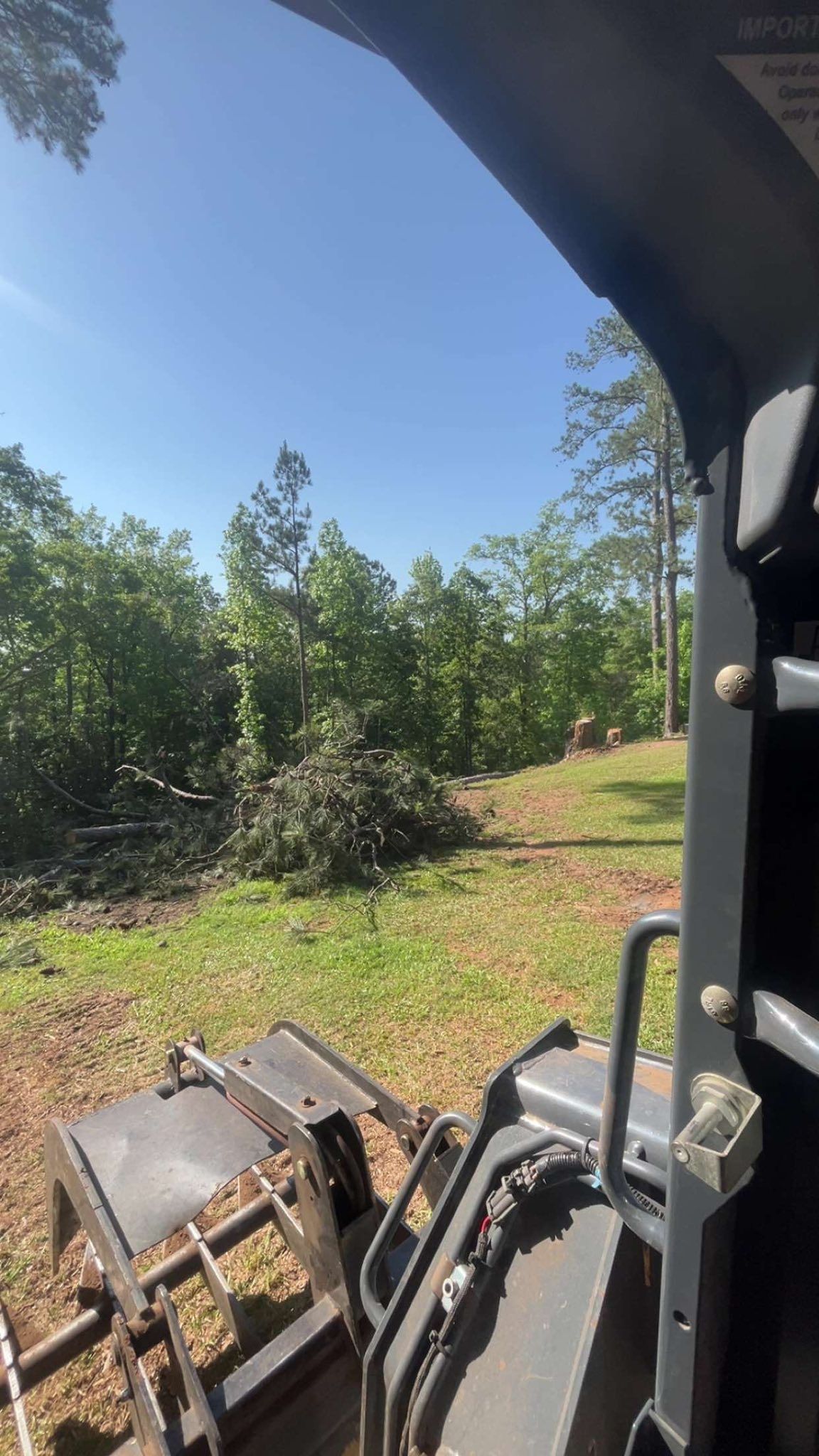 View from inside a vehicle cab of a sunny green hillside with trees and brush ahead.