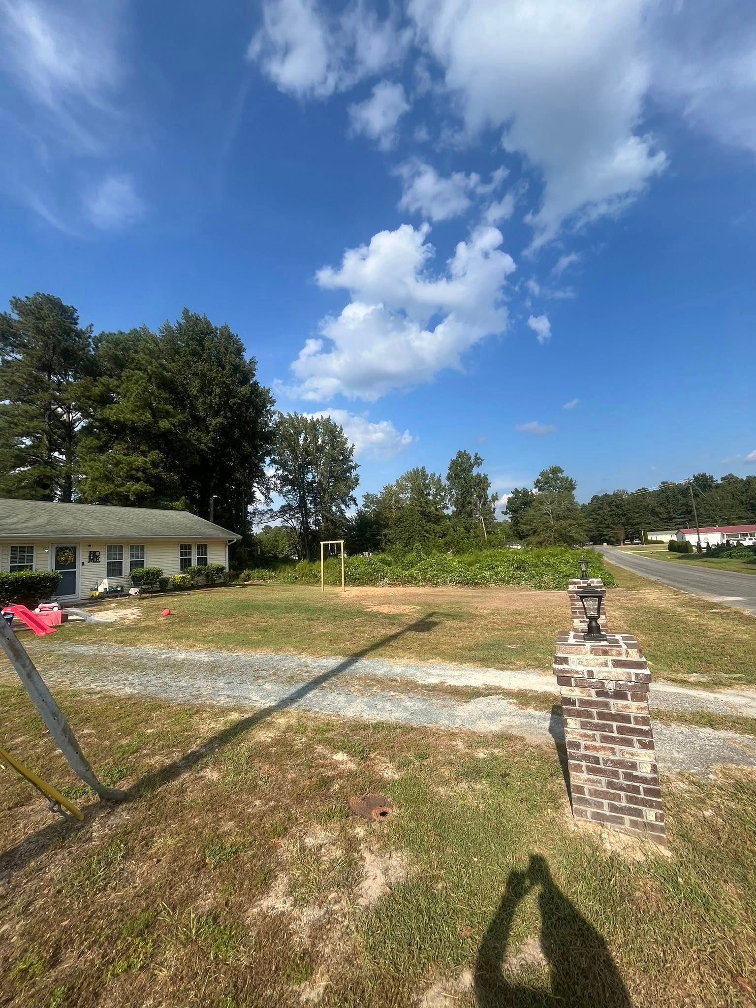 Suburban yard with a grassy lot, small house, stone mailbox, and blue sky with clouds
