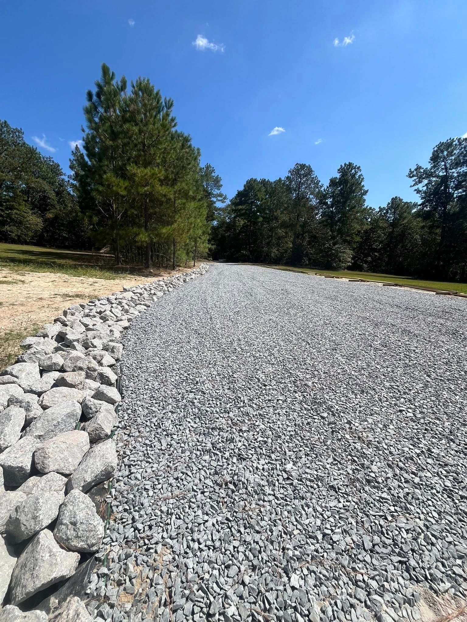 Gravel path bordered by rocks and trees under a bright blue sky