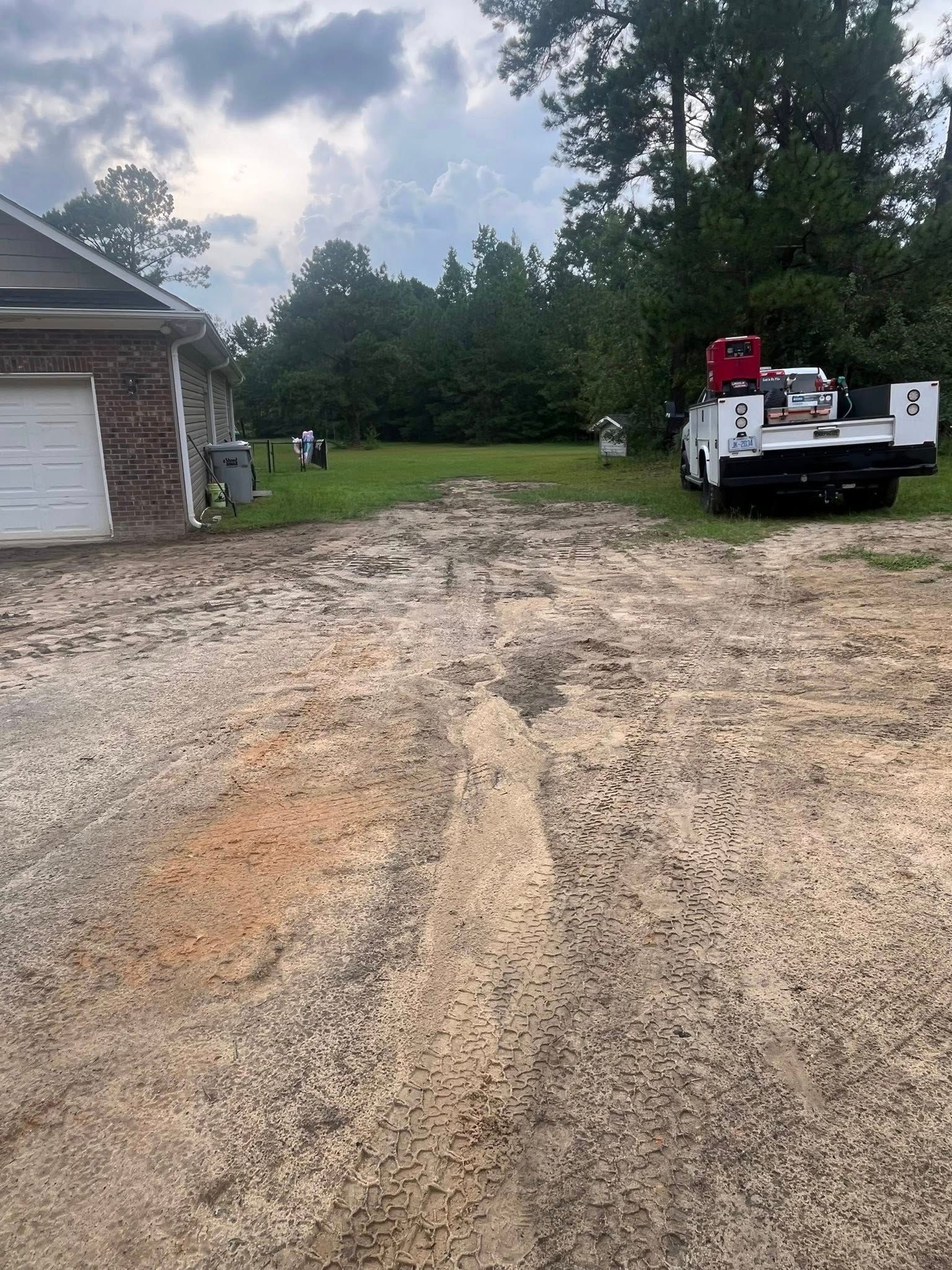 Gravel driveway beside a house with a white pickup truck and a person in a red shirt near trees.