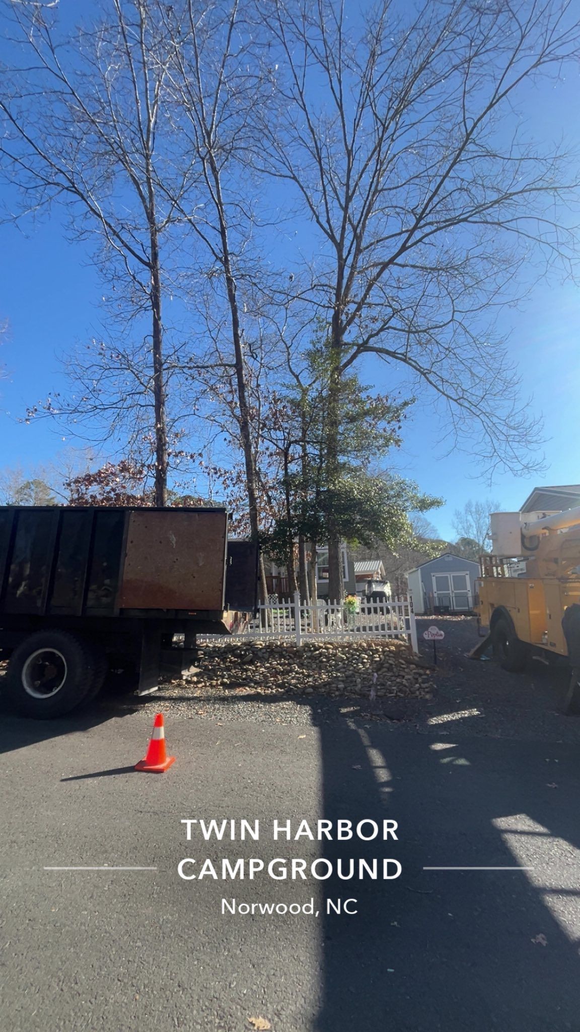 Twin Harbor Campground entrance with tall trees, parked trucks, and a traffic cone under a blue sky.