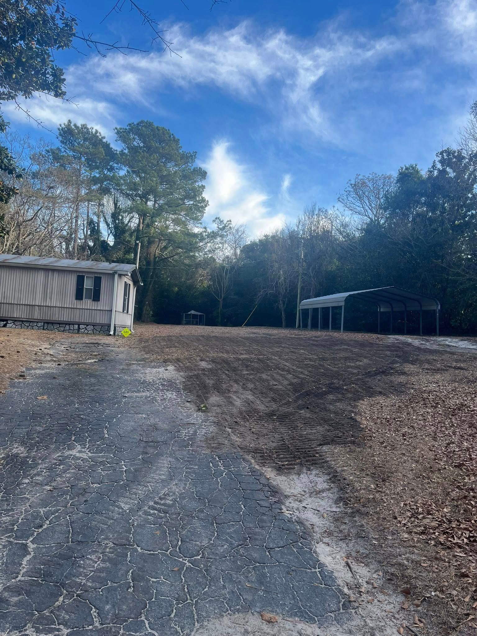 Gravel driveway leading to small buildings and trees under a blue sky with clouds
