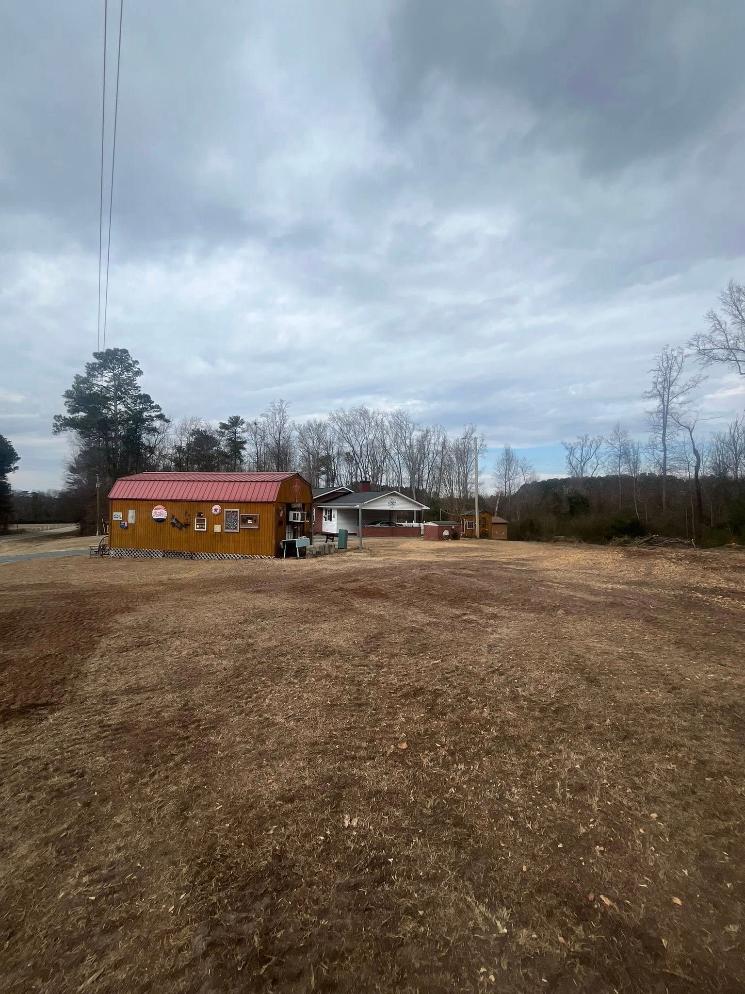 Wide gravel lot with a small red-roofed cabin under a cloudy sky, trees in the background.