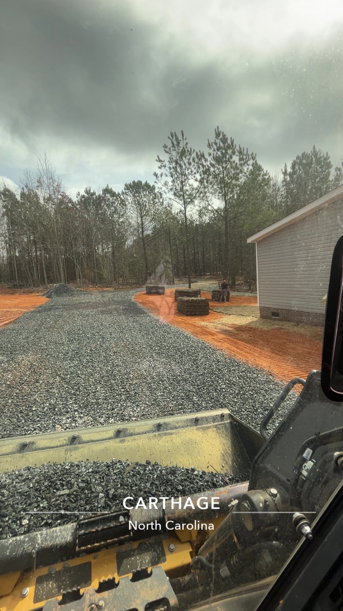 Gravel driveway beside a shed, with orange landscaping fabric and trees under a cloudy sky