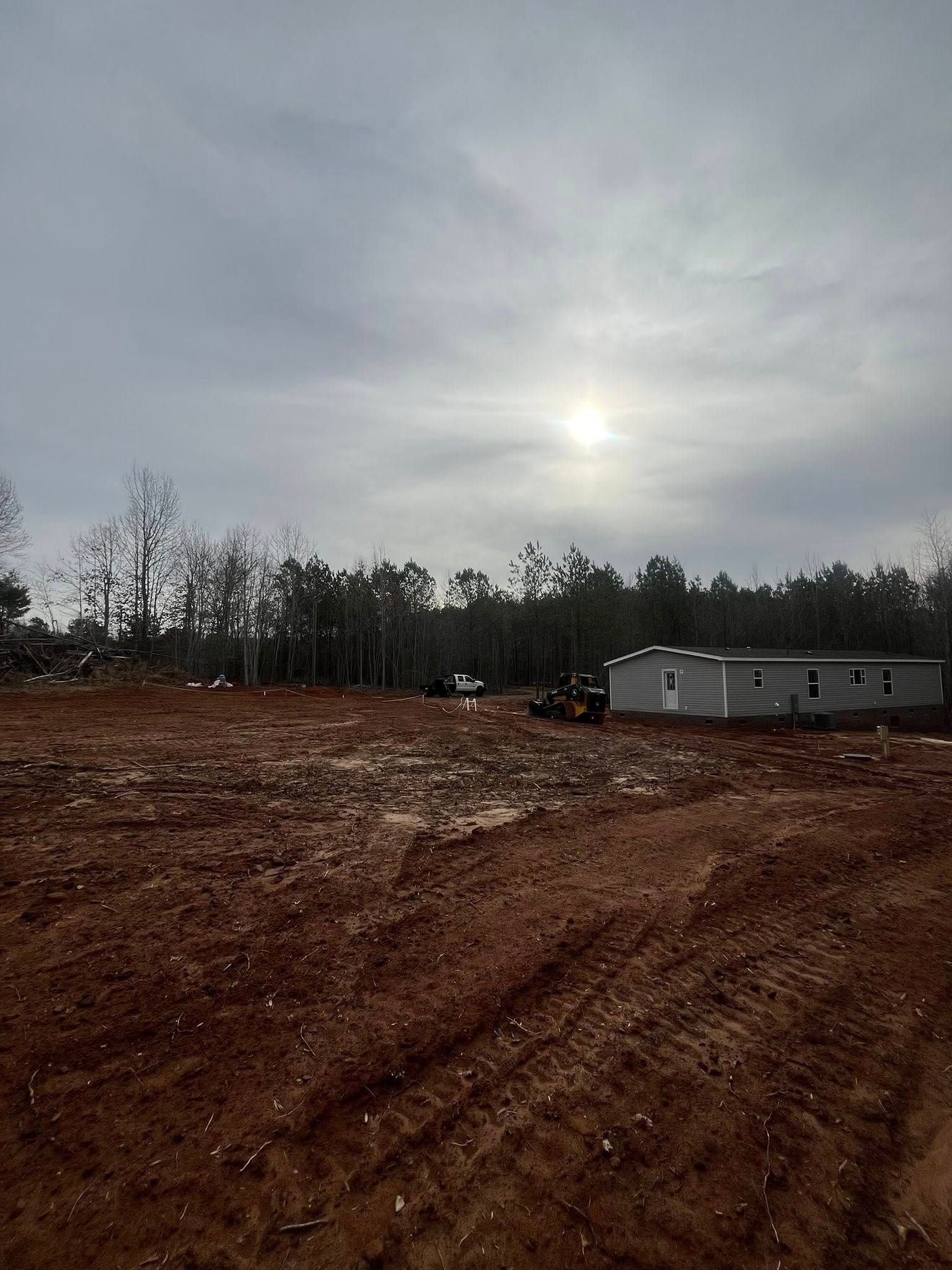 Overcast dirt lot with tire tracks, bare trees, and a gray trailer in the distance