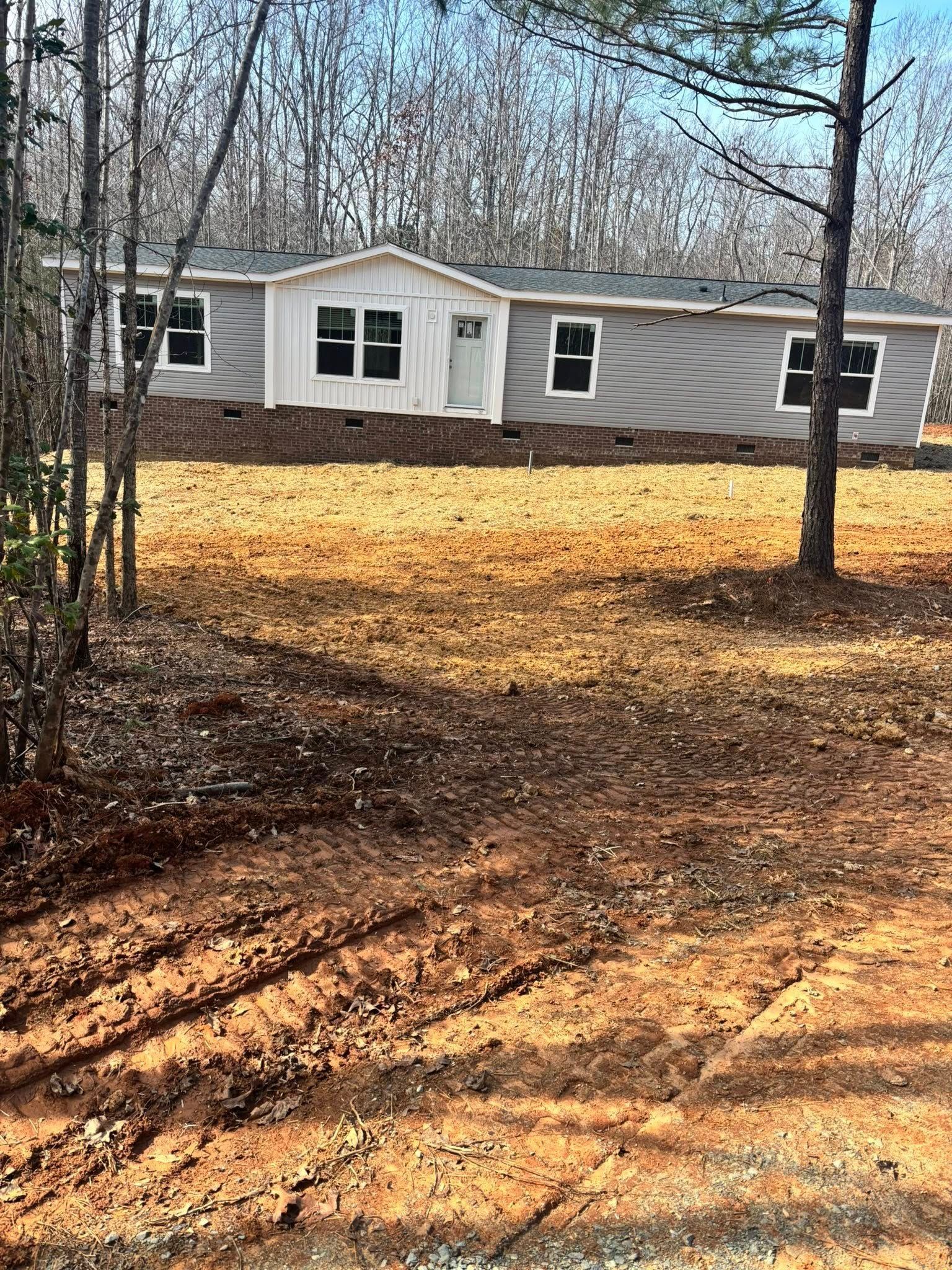 Single-story gray house with white trim in a wooded yard with fallen leaves and bare trees