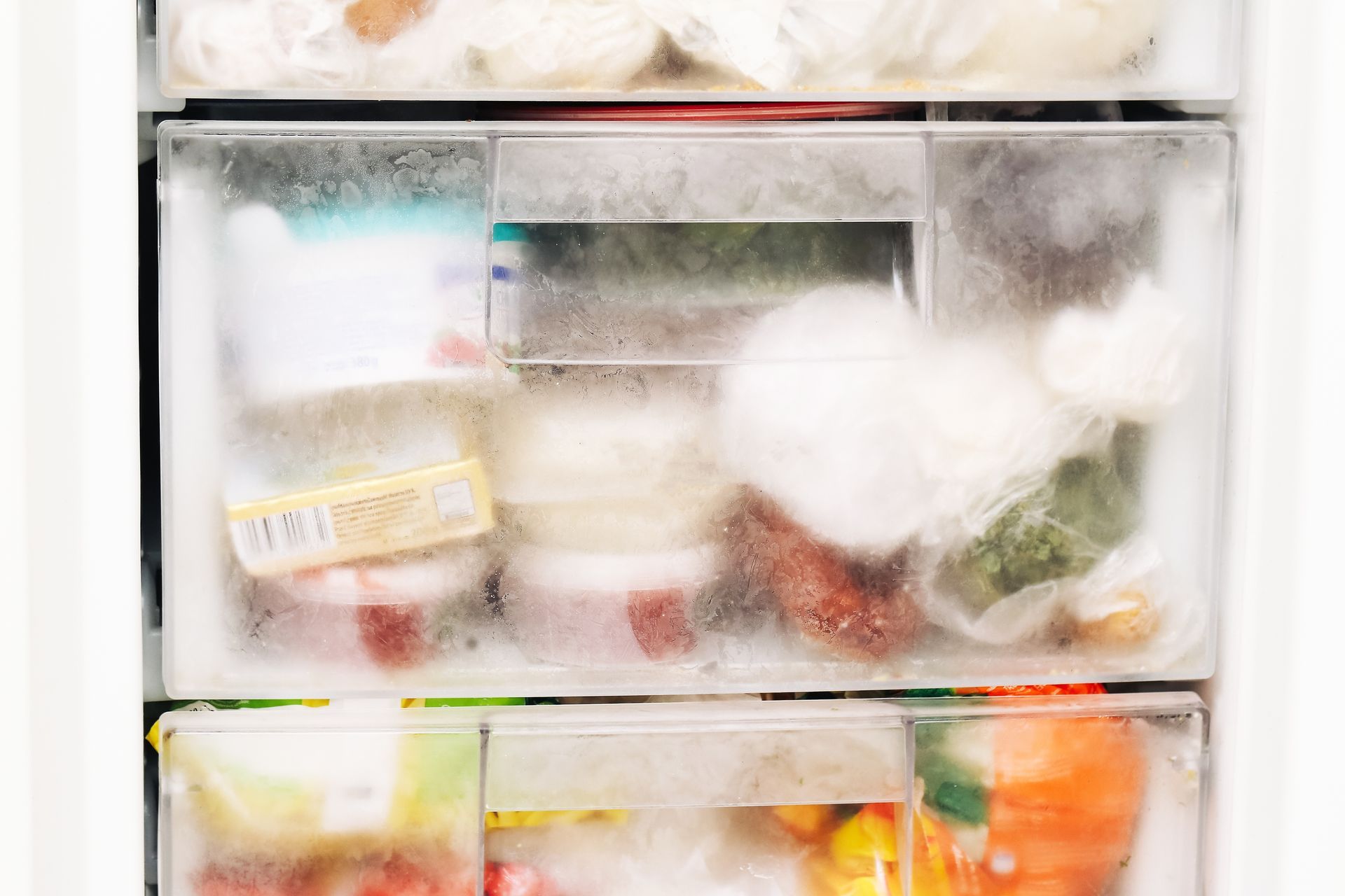Open refrigerator drawers packed with assorted food containers, produce, and ice frost.