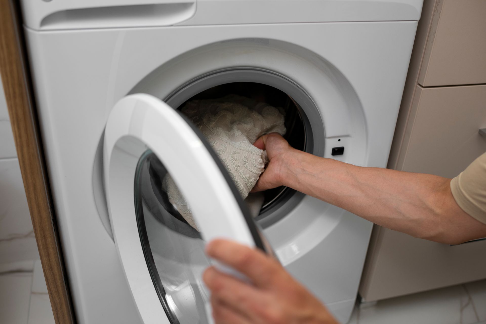 Person loading a white towel into a front-loading washing machine
