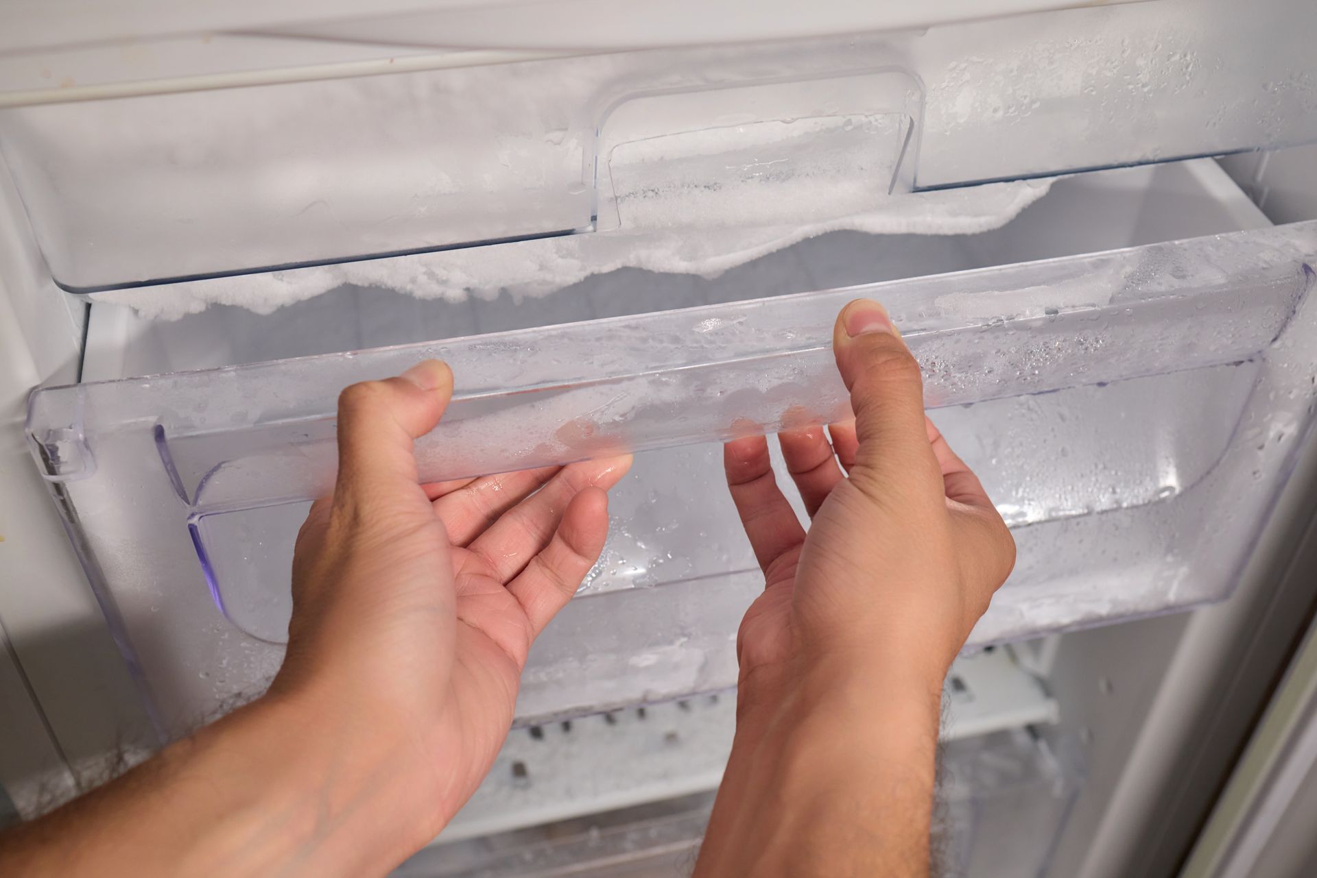 Hands holding a clear plastic shelf inside a frosted freezer.