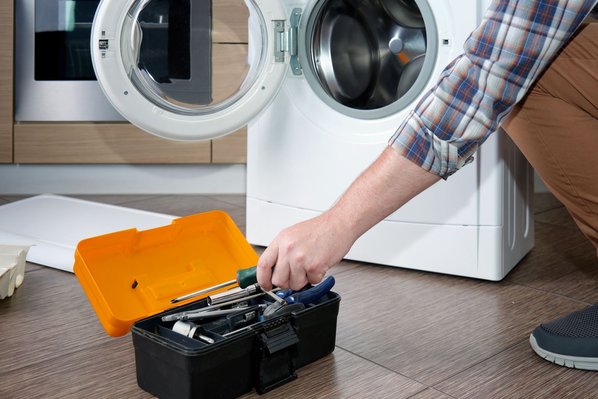 Person with toolbox repairing washing machine. Open door reveals drum.