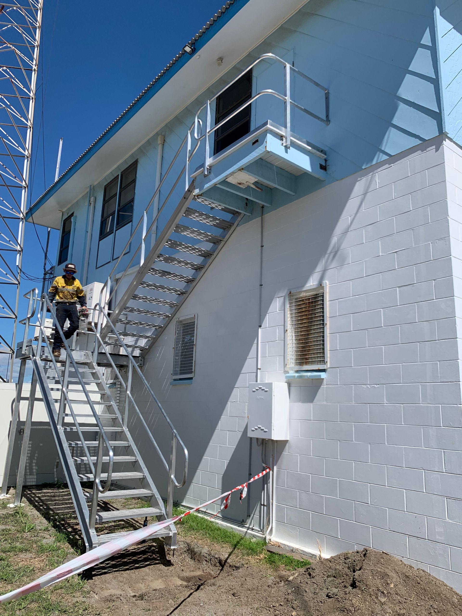 Worker On a Ladder Painting a White Brick Building with Blue Trim and Stairs — Kaplan Engineering Pty Ltd In Bowen, QLD