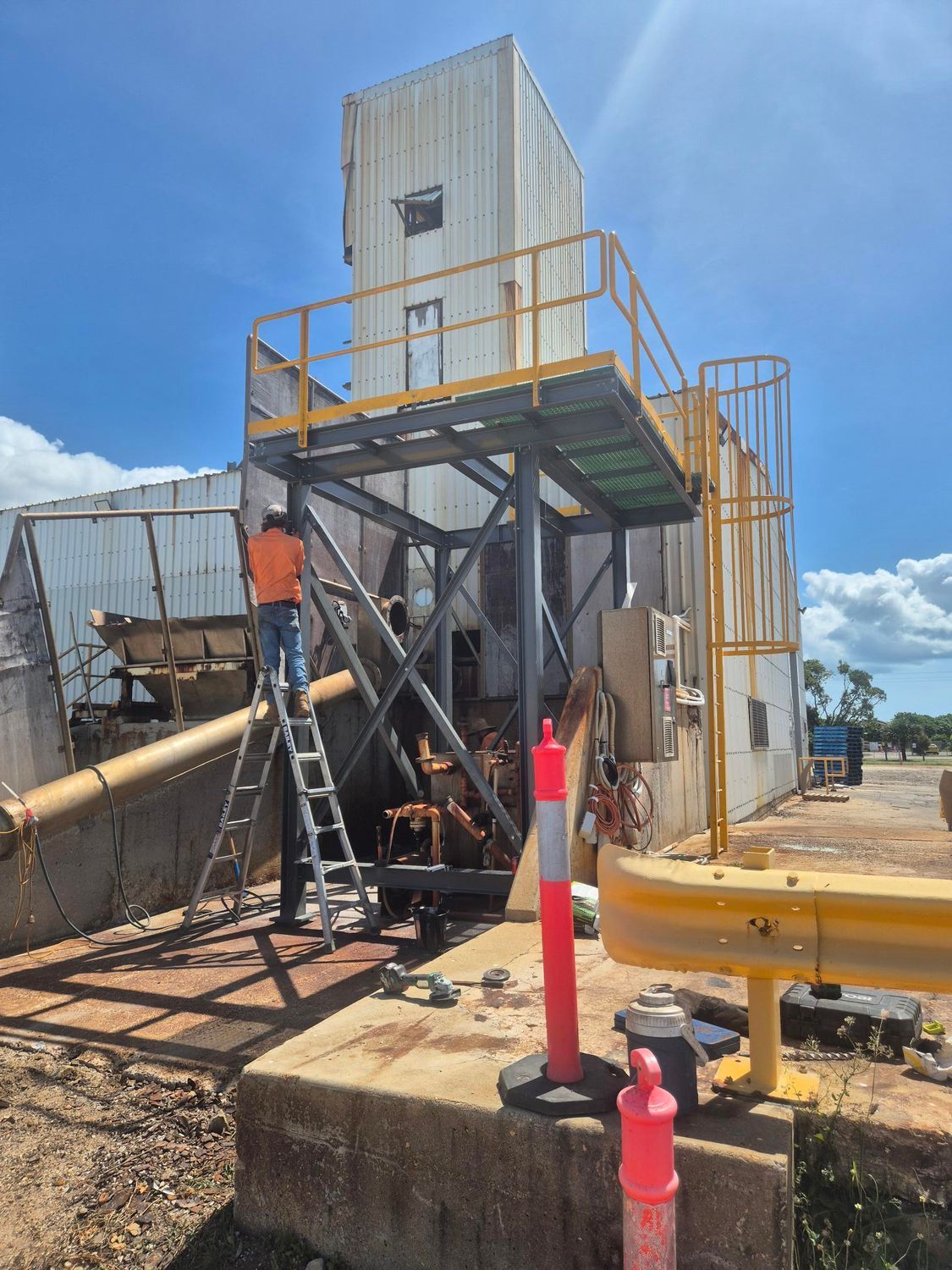 Worker On Ladder Beside Industrial Metal Machinery with Orange Railings and Hoses — Kaplan Engineering Pty Ltd In Bowen, QLD