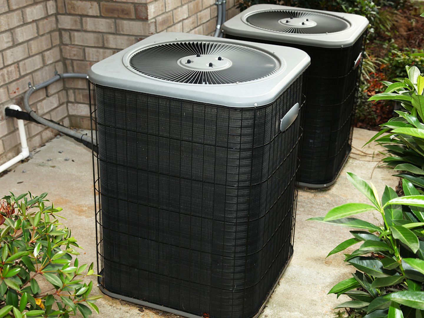 Two air conditioners are sitting on the side of a brick building.