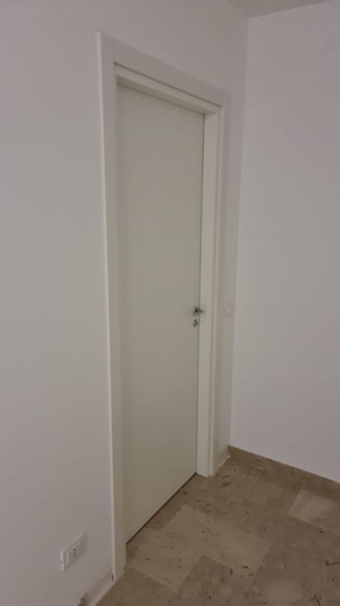 Porta interna bianca in una stanza con pareti bianche e pavimento con motivi in ​​marmo.