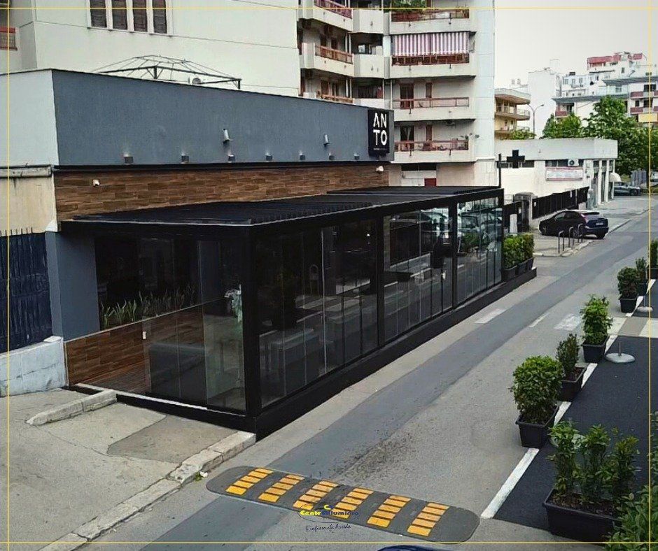 Esterno del ristorante con cornice nera, pareti in vetro, pannelli in legno e vista sulla strada.