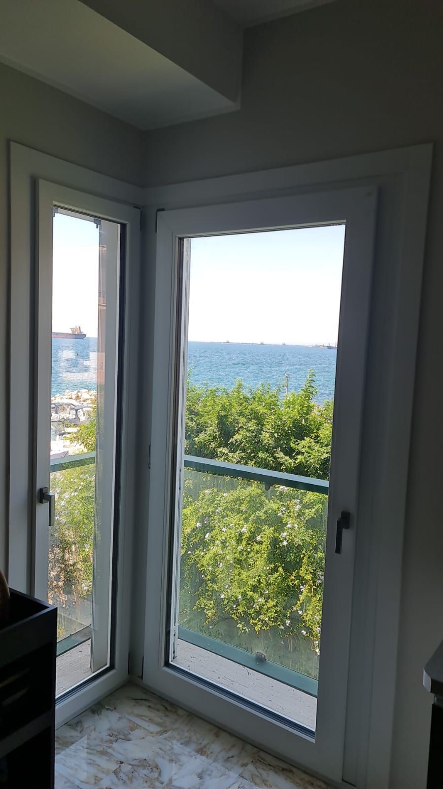Finestre angolari con vista sull'oceano e sul verde. Infissi bianchi.