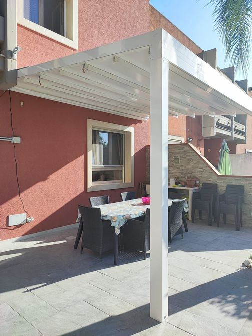 Pergola bianca sopra il tavolo da pranzo e le sedie all'aperto, contro una parete in stucco rosso.