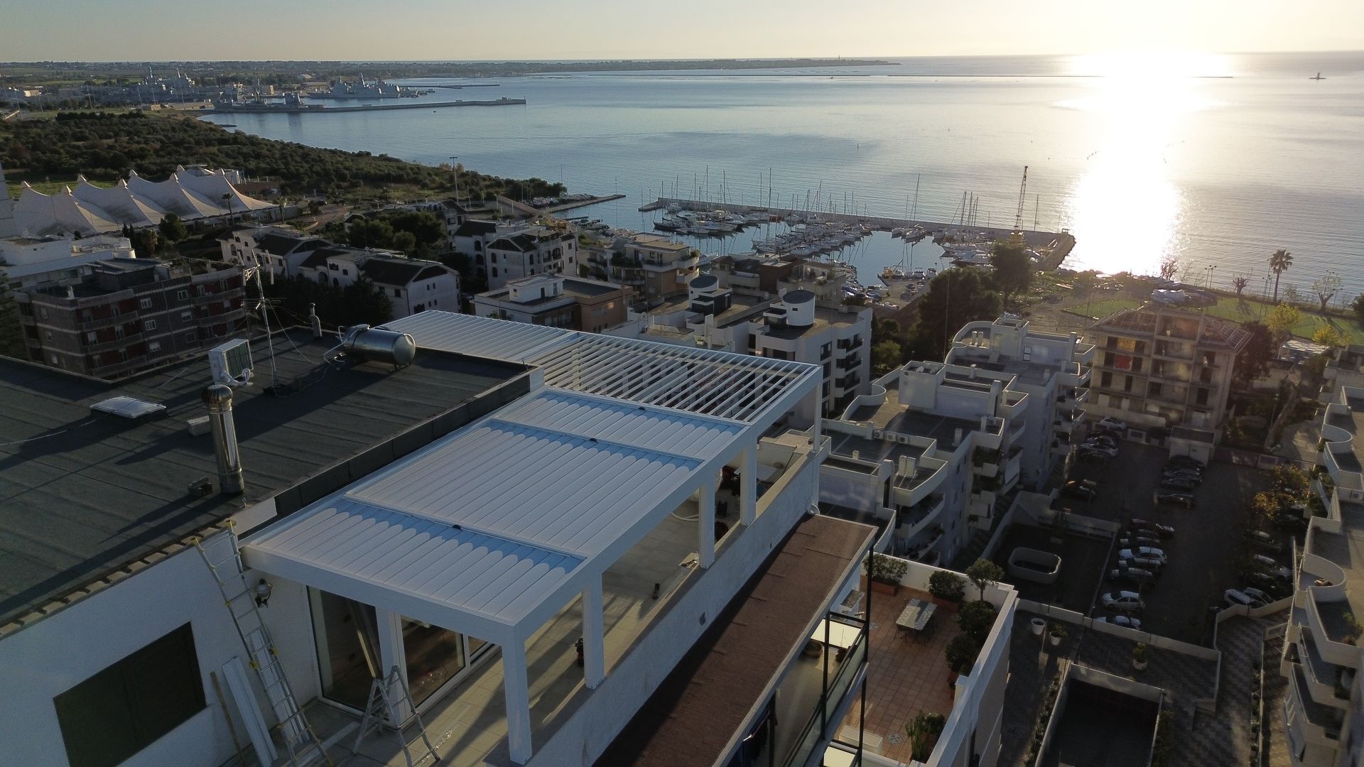 Vista panoramica della città costiera con il porto, gli edifici e l'acqua che riflette la luce del sole al tramonto.