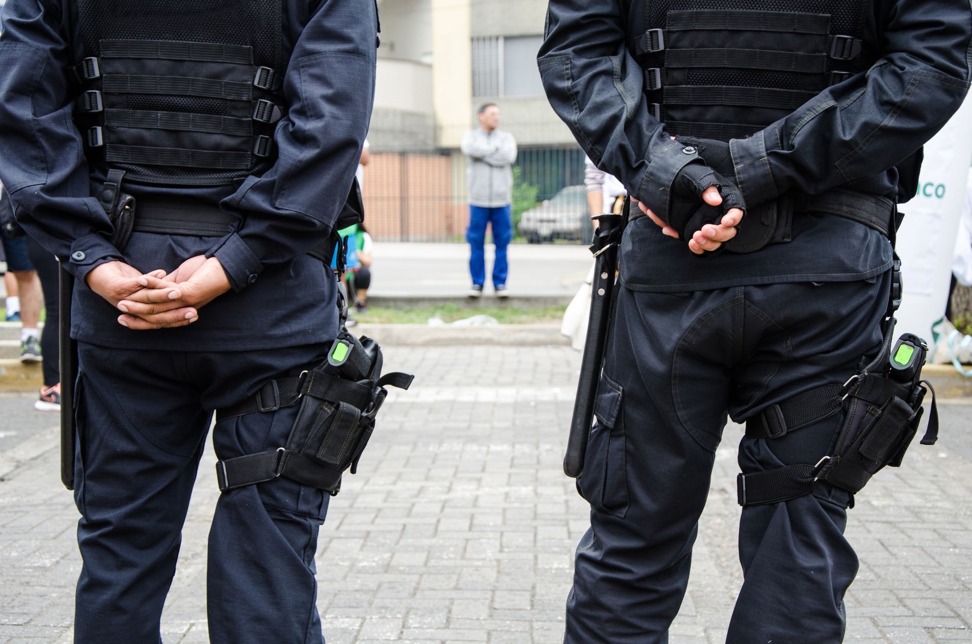Two security officers standing outdoors with protective gear and utility equipment. Two security officers standing outdoors with protective gear and utility equipment.