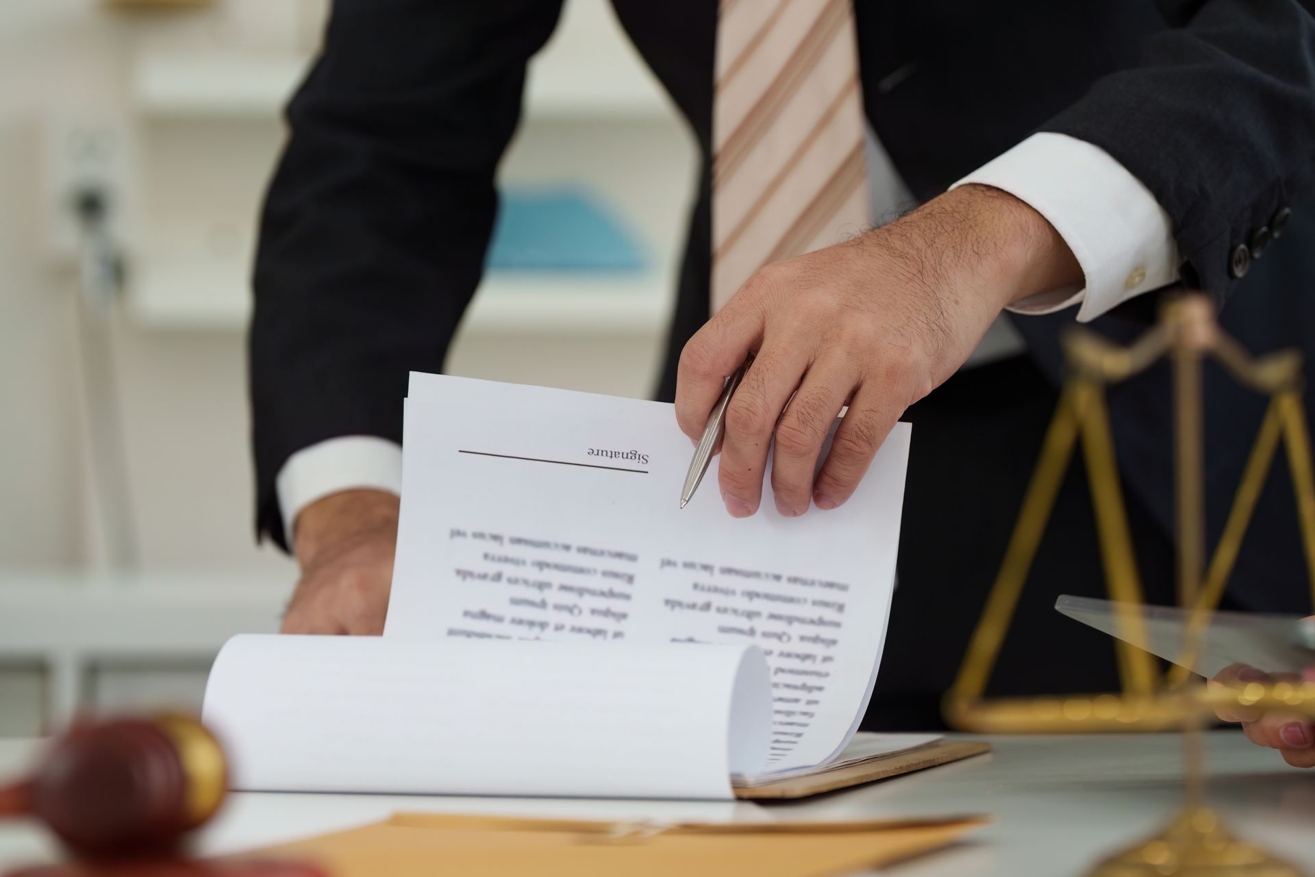 Person in a suit signing a document at a desk with a gavel and scales of justice nearby