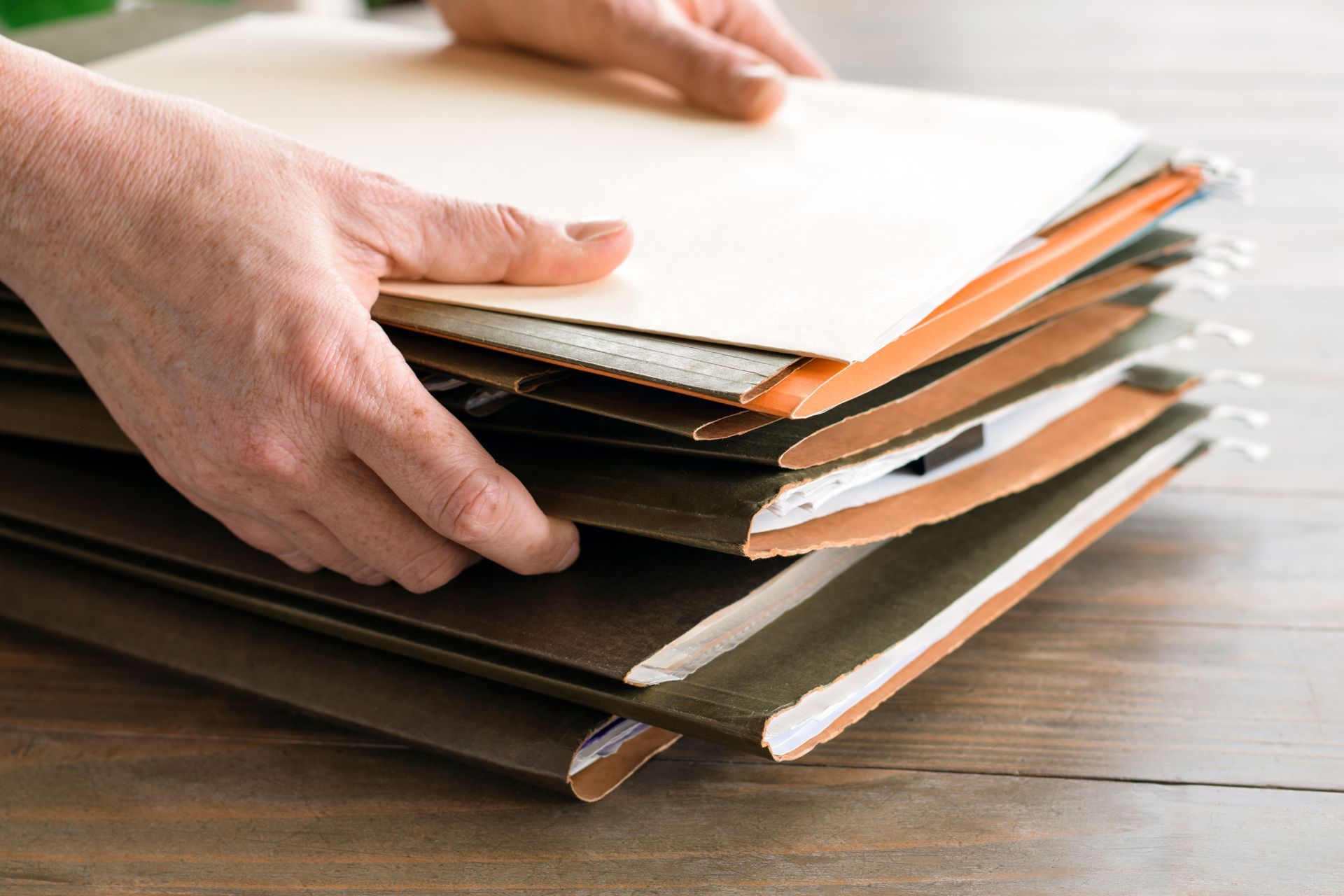 Hands sorting a stack of paper samples and folders on a wooden table