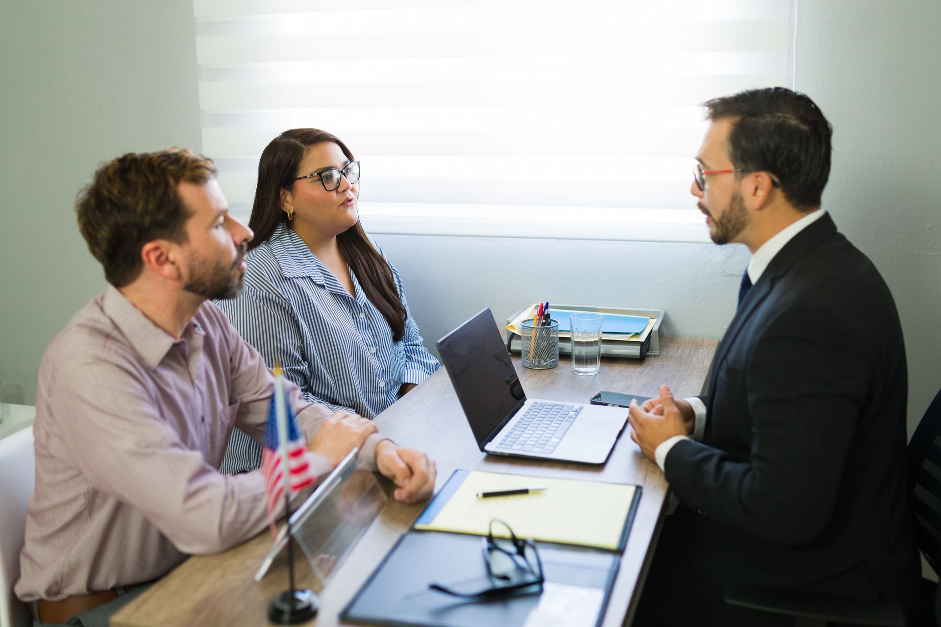 Three people in a meeting around a laptop and notebook at a table in an office