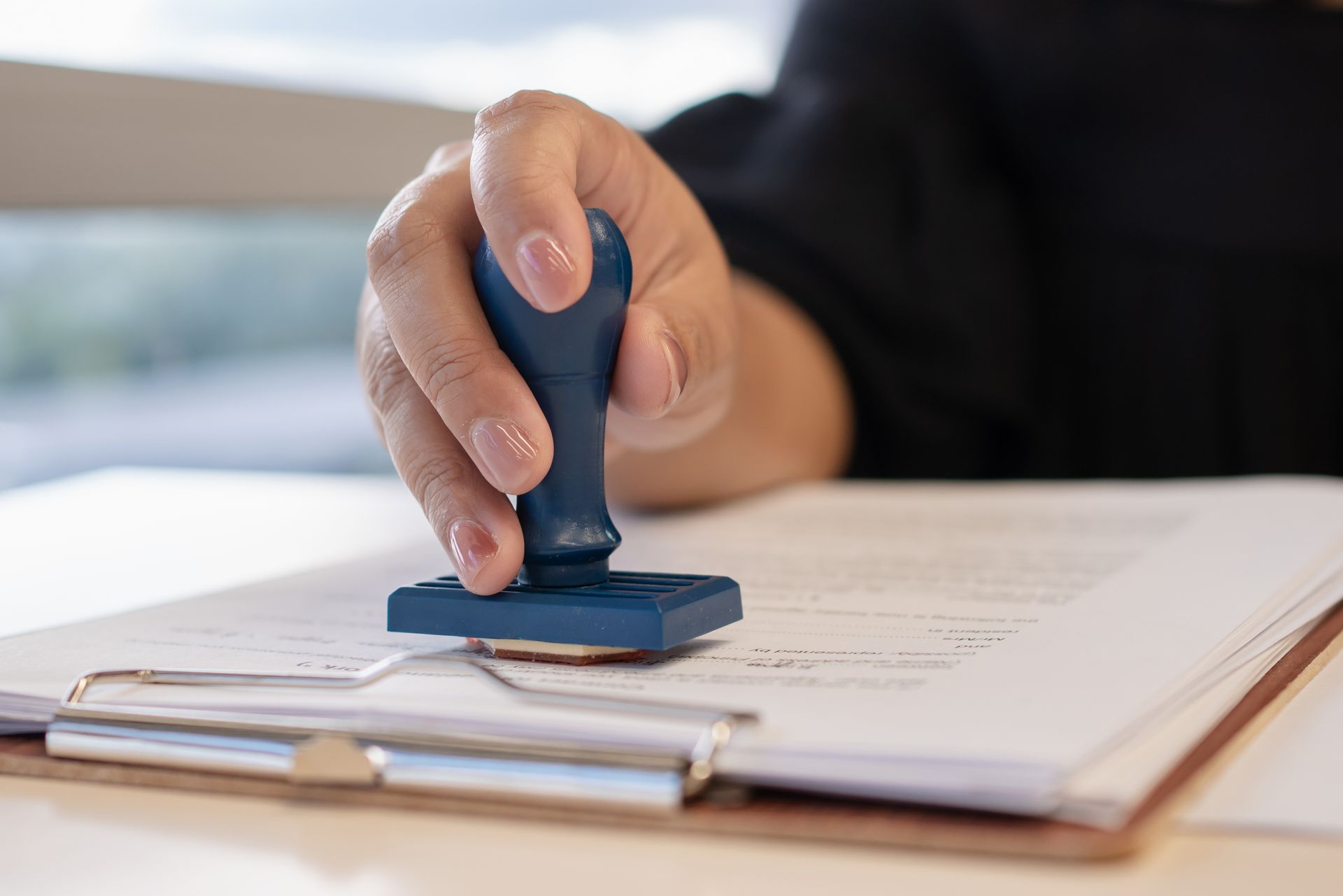 Hand stamping a document on a clipboard with a blue rubber stamp