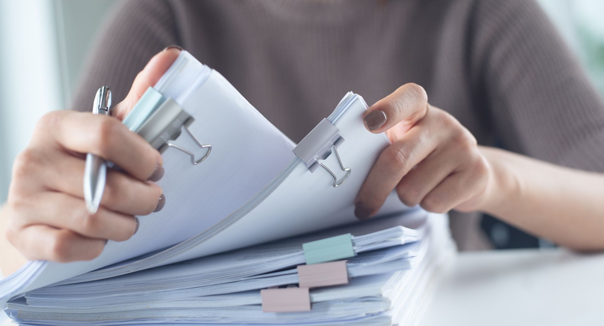 Hands turning pages in a stack of clipped documents with pastel tabs